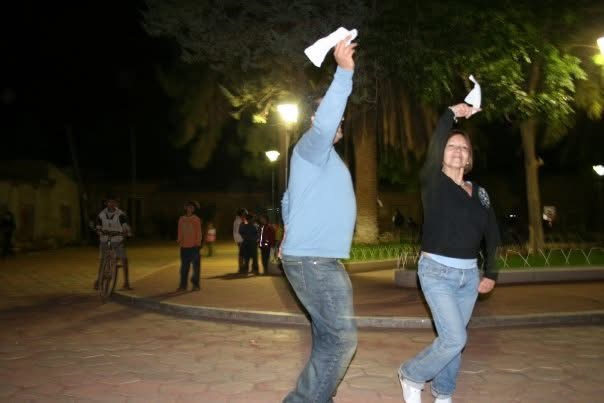 Dos personas levantan pañuelos en una plaza al anochecer.