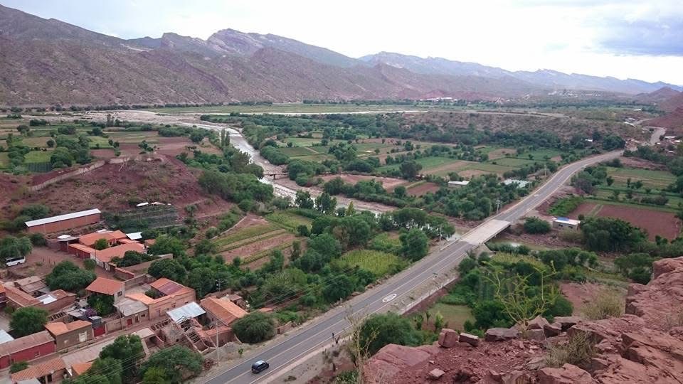 Vista elevada de un valle con un camino, un puente y cultivos entre cerros.
